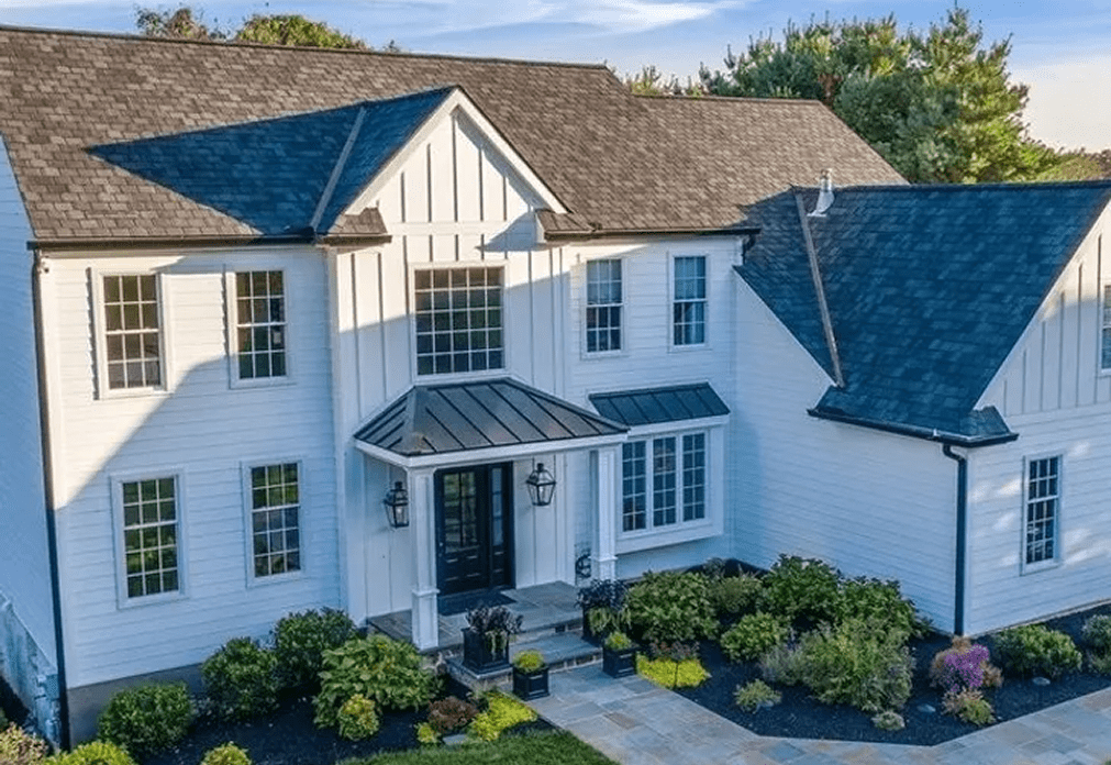 image (4) Aerial view of a modern two-story white house with black roof, large windows, a covered entryway, and landscaped front yard.