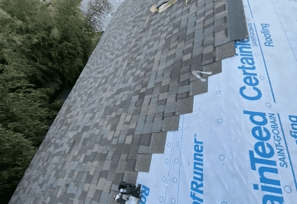 image (6) Partial roof covered with brown asphalt shingles; remaining area is covered with synthetic underlayment labeled "CertainTeed." Tools are placed on the roof.