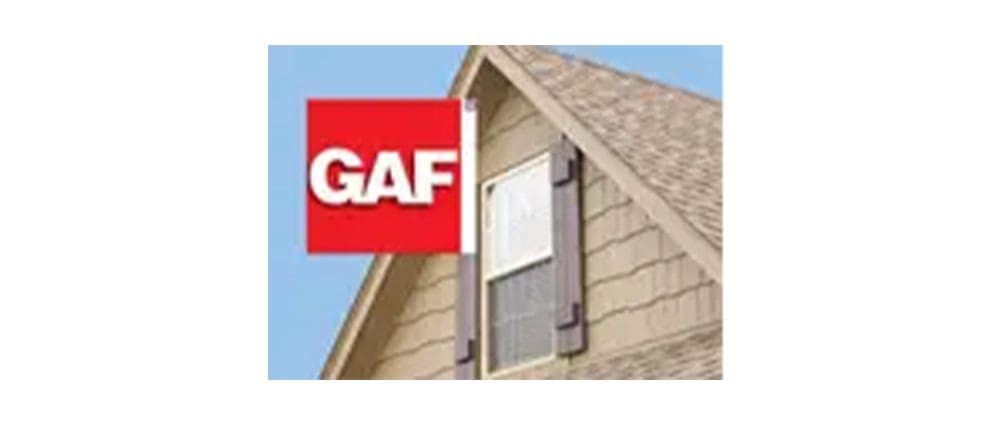 A red GAF sign is mounted on the gable of a house with beige siding and a shingled roof.