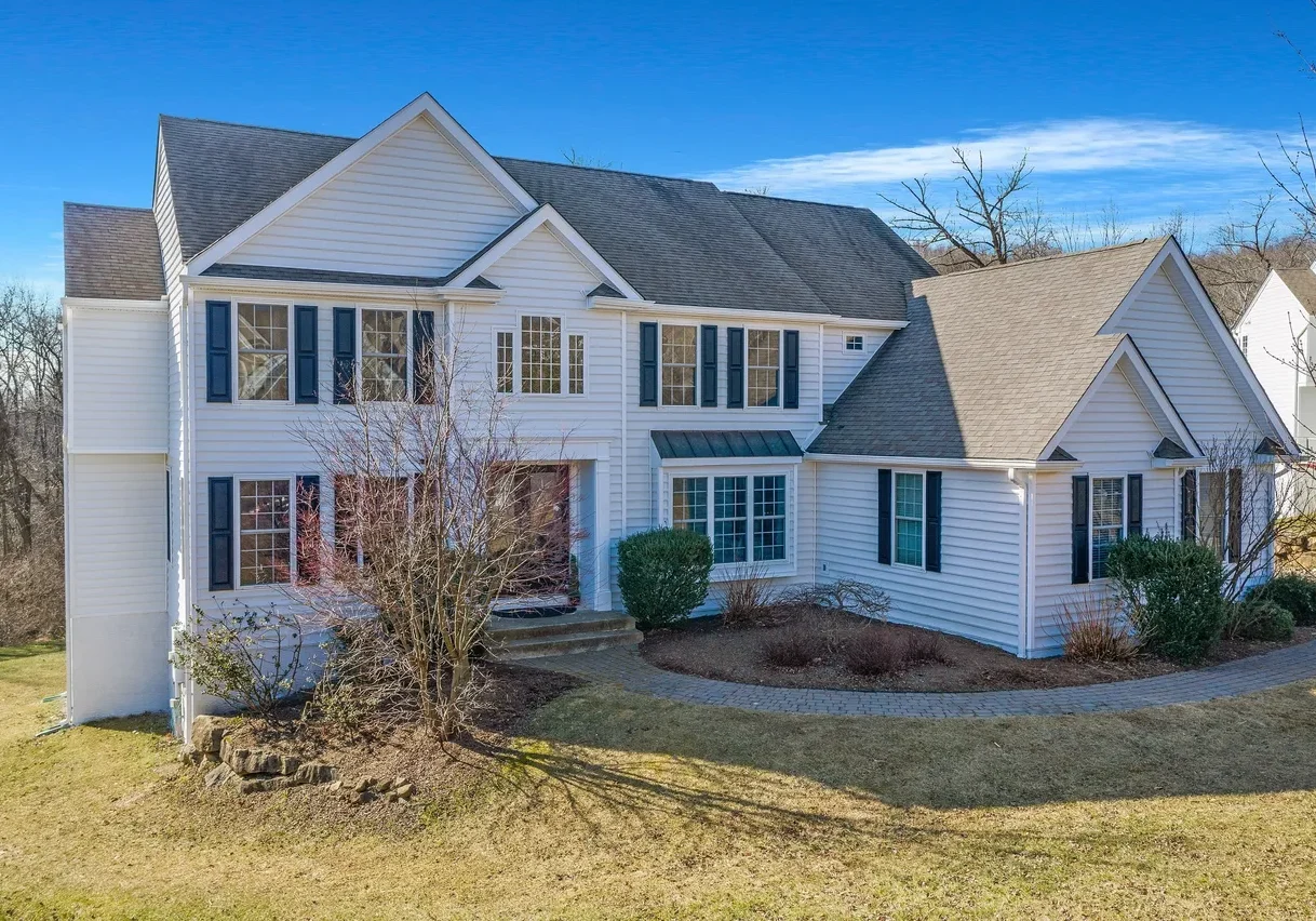 rs=w_1279,m (1) Two-story white house with dark shutters, gable roof, and minimal landscaping, set on a grassy lot with bare trees and clear blue sky in the background.
