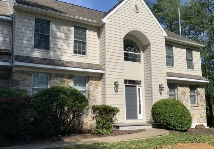 rs=w_1279,m (2) Two-story suburban house with light siding, stone accents, central arched entryway, double front doors, and bushes in front under a partly cloudy sky.